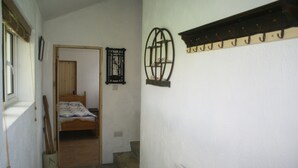 A narrow hallway with a wooden door leading to a bedroom with a bed and a window. There is a coat rack on the wall and a radiator on the right side. - Beautiful house with garden that runs down to the sea (Cashel)