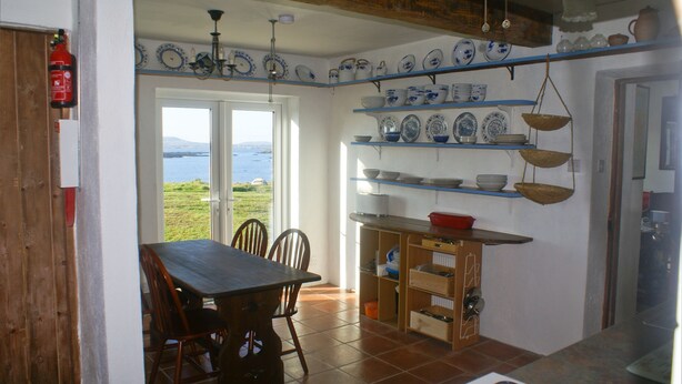 A kitchen with a dining table, chairs, and a view of the sea through a door. - Beautiful house with garden that runs down to the sea (Cashel)