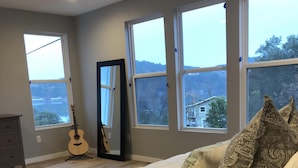 Ein Schlafzimmer mit einem großen Bett, mehreren Fenstern, einer Gitarre und einem Deckenventilator.