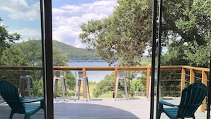 Ein Zimmer mit Blick auf einen See und Hügel, ausgestattet mit einer Holzterrasse, zwei Stühlen und einem kleinen Tisch.