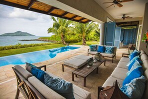 A poolside area with a view of the ocean, a lounge with sofas and a table, and a ceiling fan. - Luxury private villa on Eden Island (Victoria)