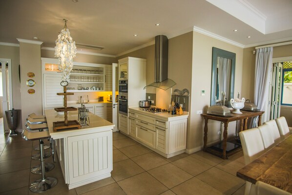 A spacious kitchen with a central island, a dining area with a wooden table, and a large window with curtains. - Luxury private villa on Eden Island (Victoria)