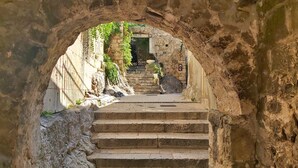 A stone staircase leading through an arched doorway, with a view of a building entrance and a sign indicating a location. - Holiday house with private pool in a quiet location (Podašpilje)