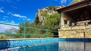 A clear blue pool with a stone wall and a balcony overlooking a mountainous landscape. - Holiday house with private pool in a quiet location (Podašpilje)