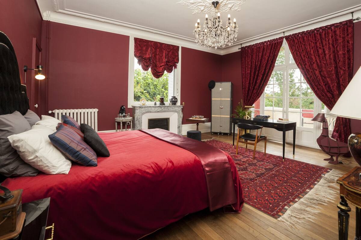 Een slaapkamer met een groot bed, een bureau, een stoel, een open haard en een kroonluchter.