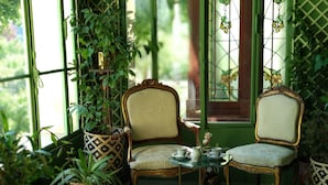 A conservatory with two ornate chairs, a small table, and potted plants. - Villa Alecya (Sainte-Catherine-de-Fierbois)