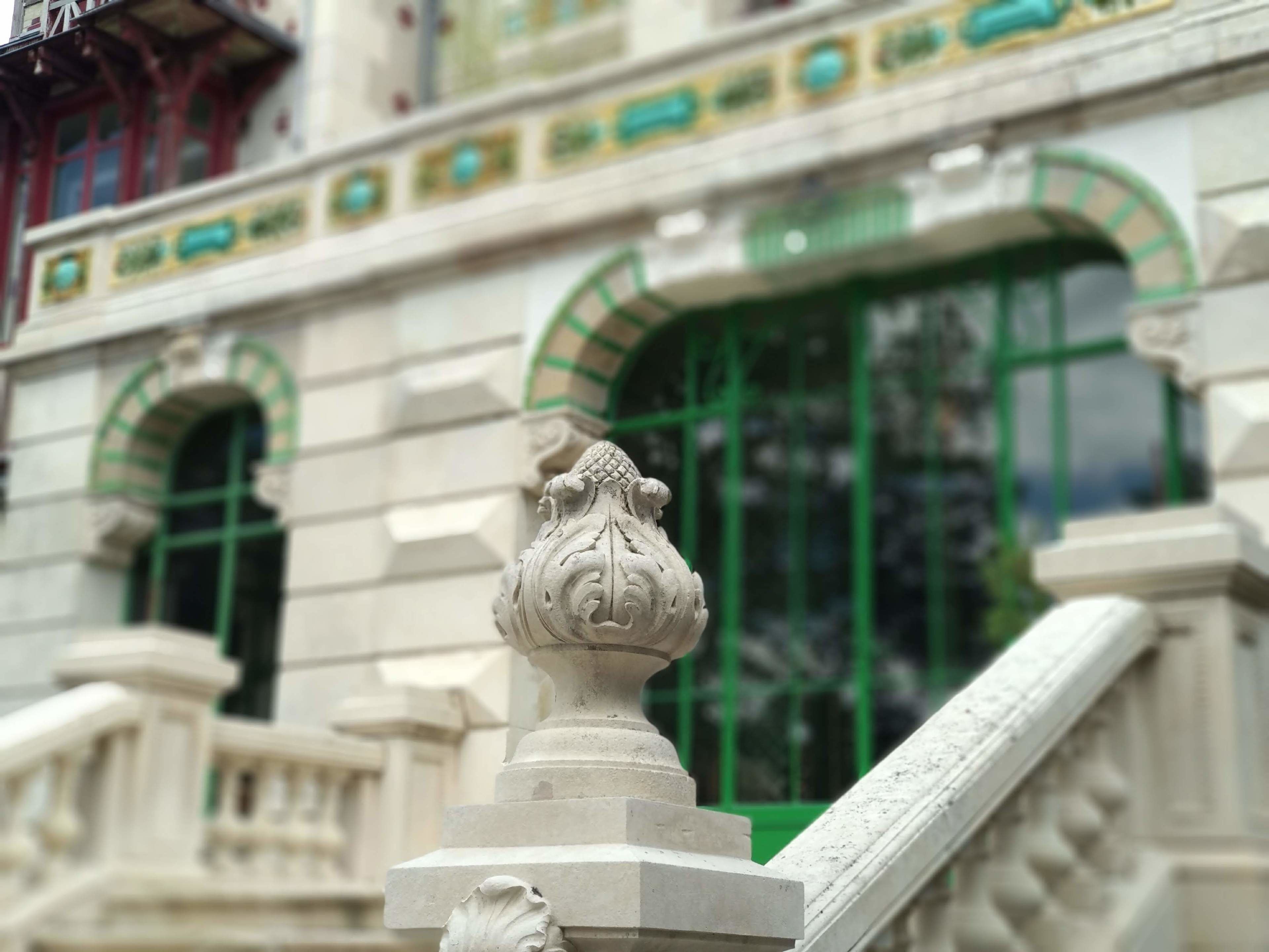 Une balustrade en pierre ornée de sculptures complexes et une fenêtre verte à arc.