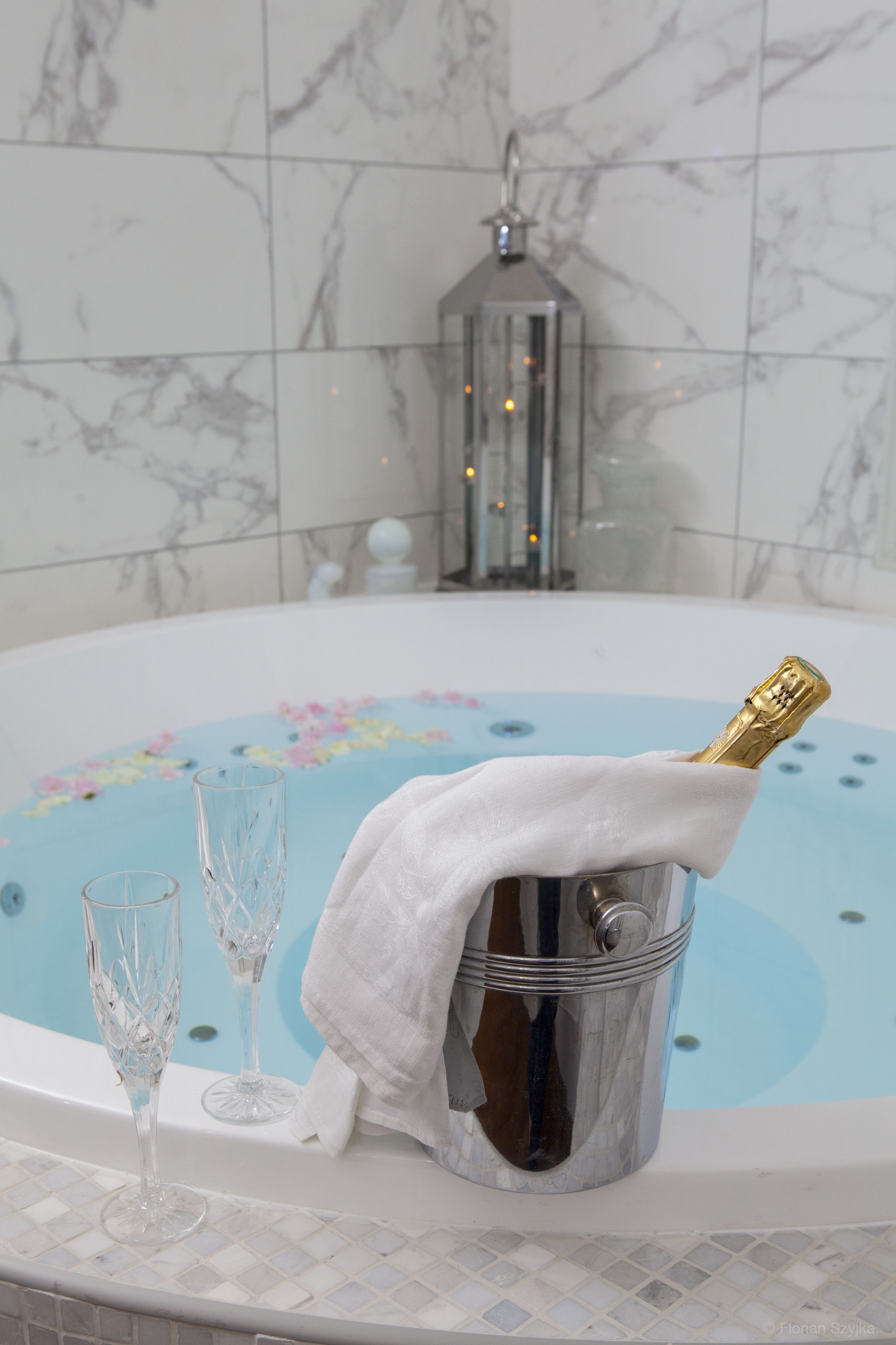 A bathtub with a floral design, a champagne bottle in a bucket, and two crystal glasses.