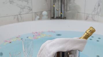 A bathtub with a floral design, a champagne bottle in a bucket, and two crystal glasses.