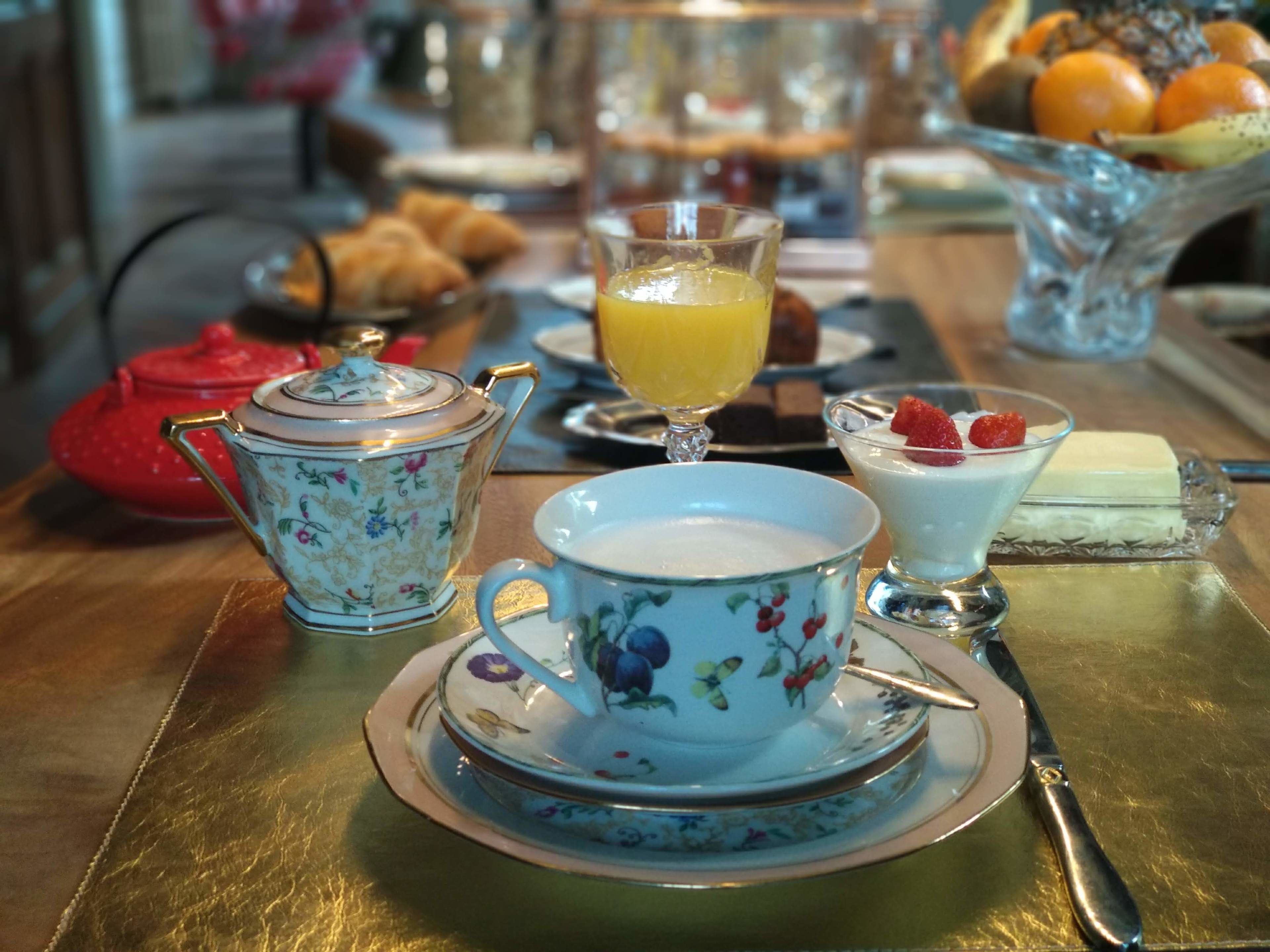 A breakfast setting with a teapot, cup, and saucer, a glass of orange juice, a bowl of strawberries, and a dessert plate.