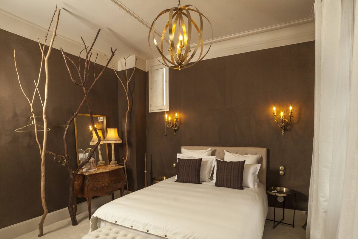 Een slaapkamer met een groot bed, een bankje, een kaptafel, een spiegel en wandlampen.