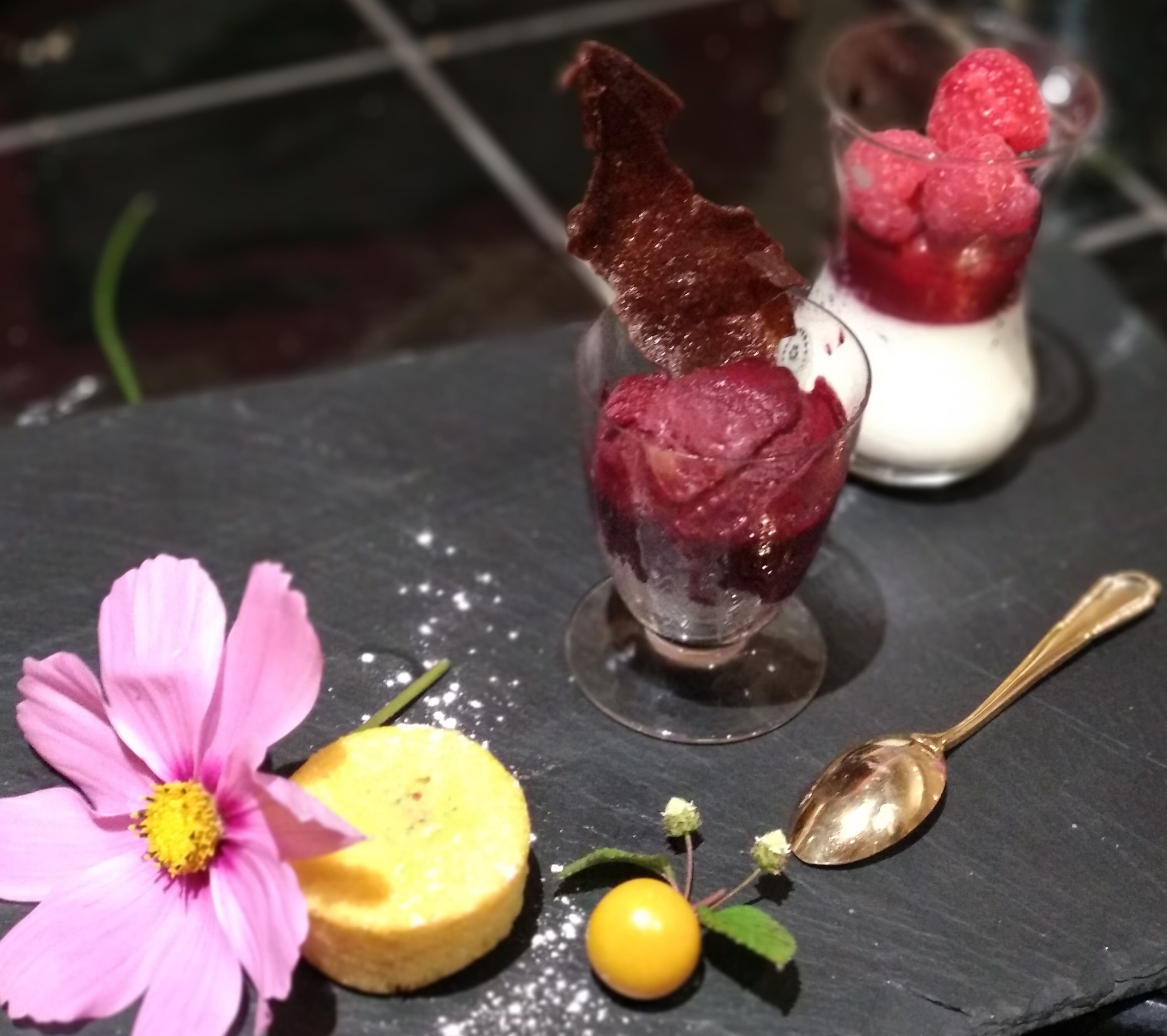 A dessert plate with ice cream, a flower, and a fruit on a slate table.