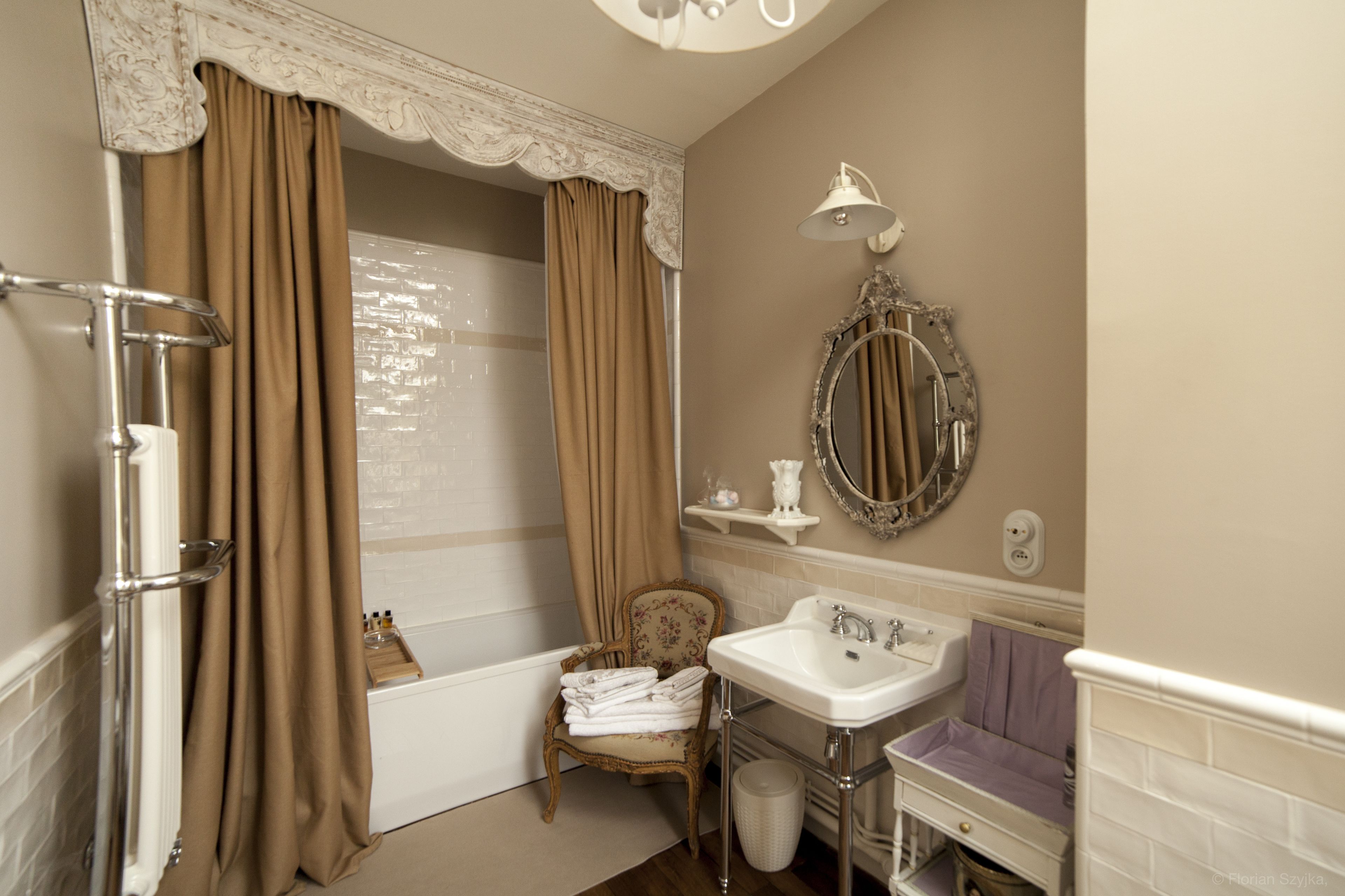 Ein Badezimmer mit einer Badewanne, einem Waschbecken, einem Stuhl mit Handtüchern und einem Spiegel an der Wand.
