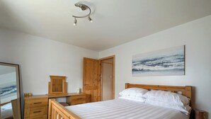 Une chambre à coucher avec un lit en bois, une commode en bois, une armoire en bois, un miroir et un tableau accroché au mur.