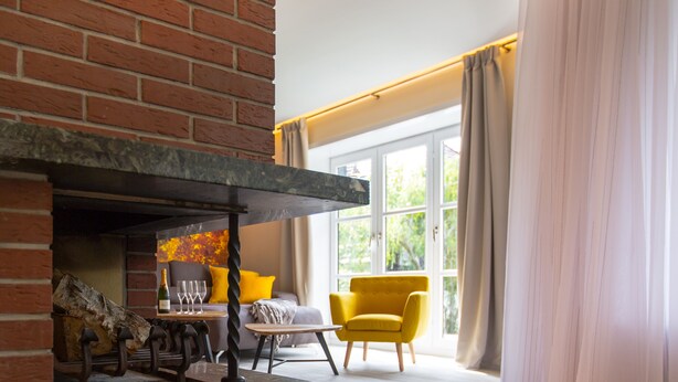 A modern living room with a fireplace, a sofa, a yellow armchair, and a dining table with glasses and a bottle. - "Waldblick" - 90 m² oasis of tranquility: Modern design & 2 bathrooms (Bad Sachsa)