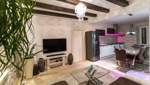 Ein modernes Wohnzimmer mit Flachbildfernseher, einem Essbereich mit Glastisch und einer Küche mit Edelstahl-Kühlschrank.