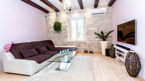 Ein modernes Wohnzimmer mit einer Steinwand, einem weißen Sofa, einem Glastisch und einem Fernseher auf einem weißen Schrank.