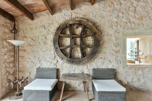 A rustic stone interior with wicker furniture, a large wooden wheel, and a hanging lamp.