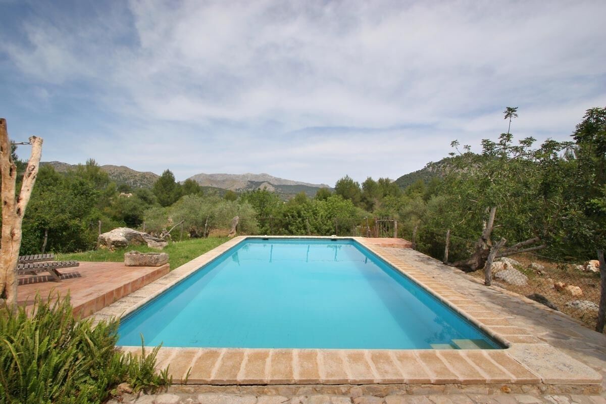 Una piscina rectangular con agua azul cristalina, rodeada de escalones de piedra y una terraza de madera.