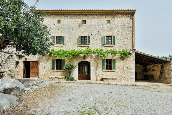 A stone building with a central entrance, multiple windows with shutters, and a gravel driveway.