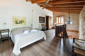 Een slaapkamer met een bed, houten vloer, plafondventilator, kunstwerken en een trap naar een vide.