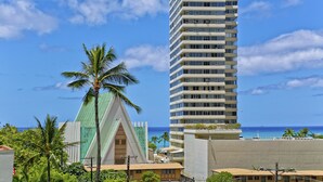 A tall hotel with multiple floors and balconies, a distinctive green and white building with a triangular roof in the foreground, and a clear view of the ocean.