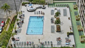 A rooftop pool with multiple swimming areas, sun loungers, and a hot tub.
