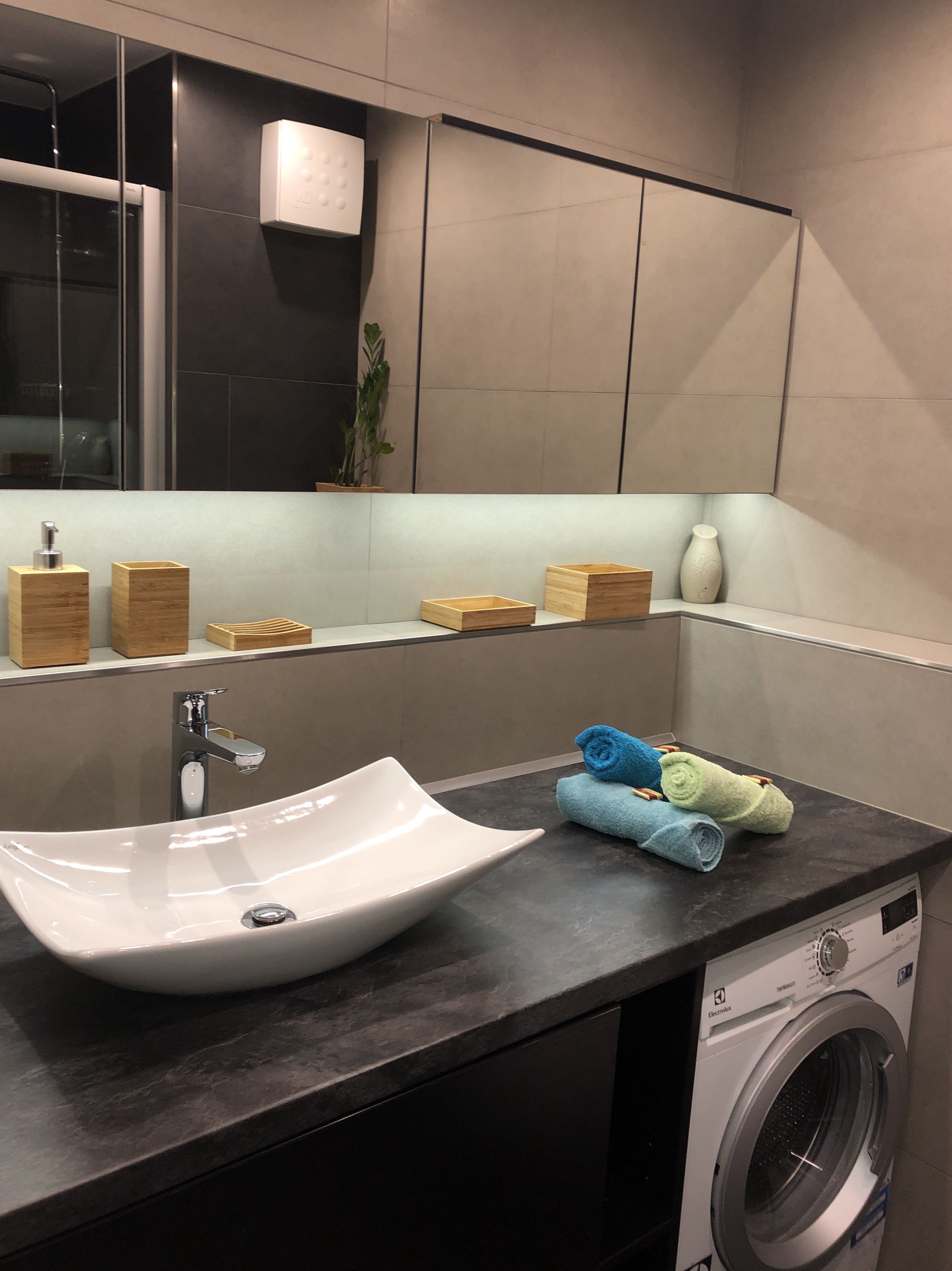 A modern bathroom with a large sink, a mirror, a washing machine, and neatly arranged towels.