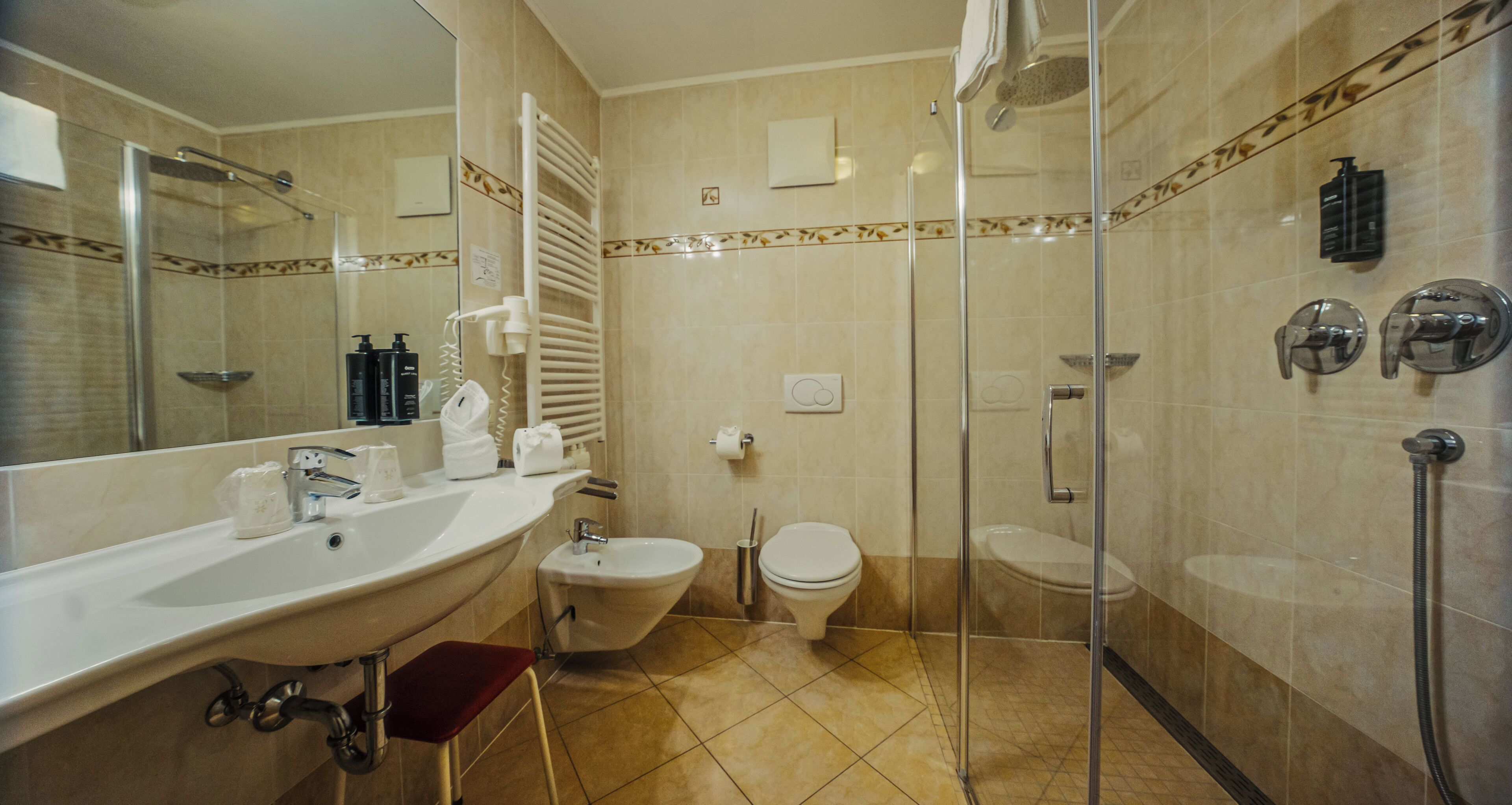 Bagno con doccia vetrata, bidet, WC e lavandino con specchio.
