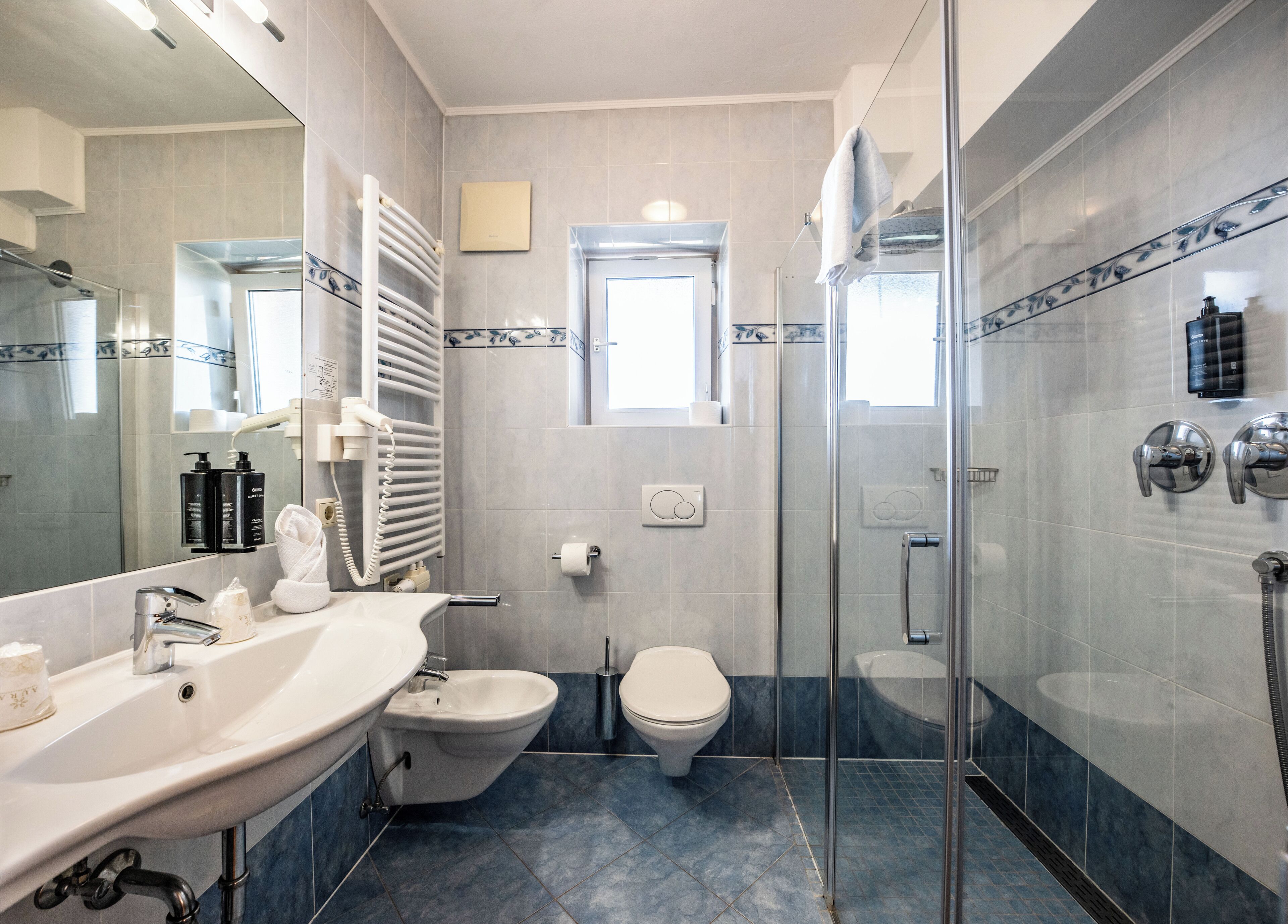 Un baño con ducha de vidrio, lavamanos blanco, inodoro y espejo.