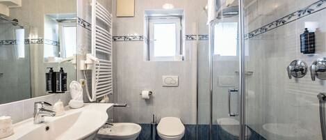 Un baño con ducha de vidrio, lavamanos blanco, inodoro y espejo.