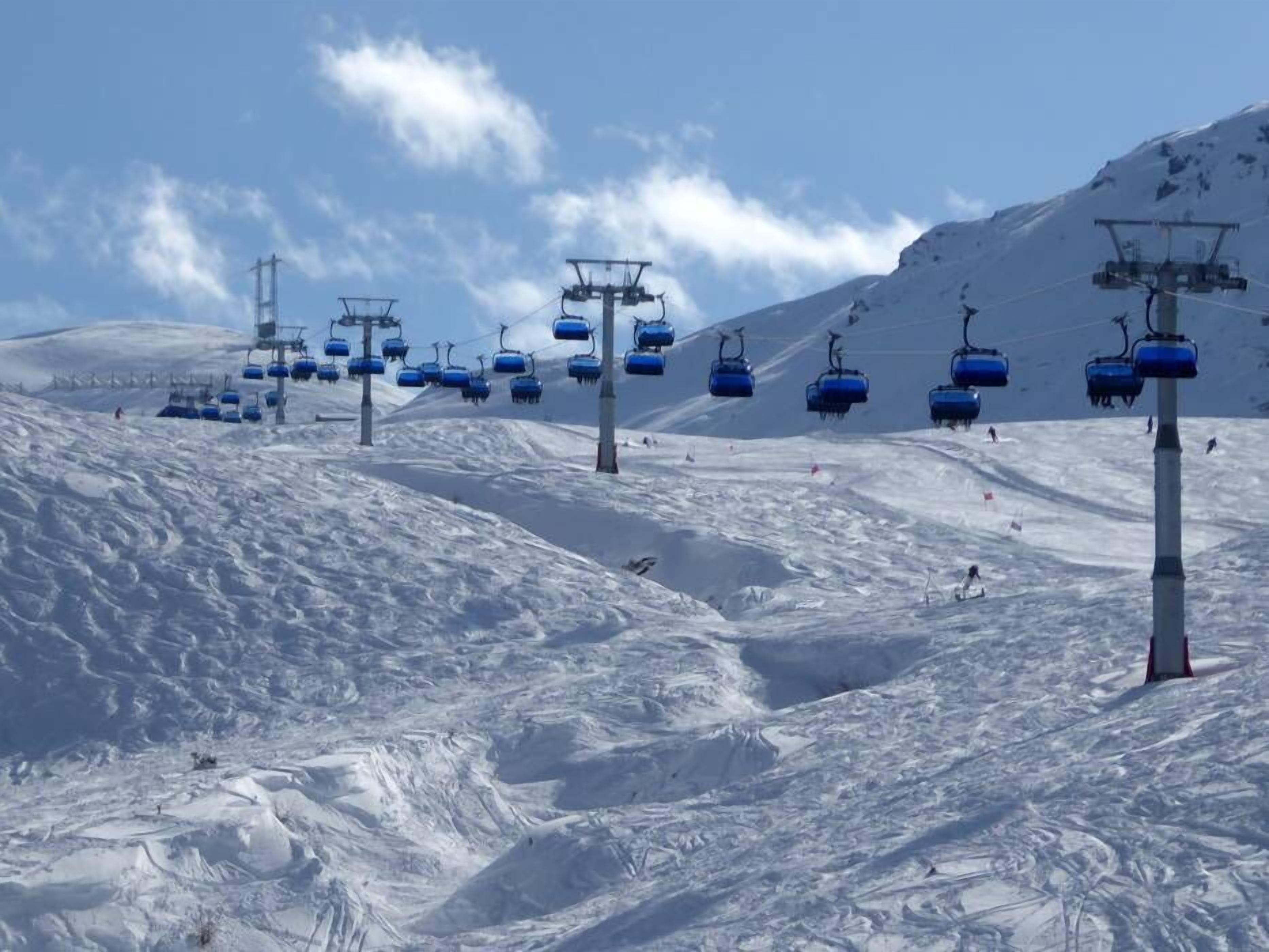 A ski lift with blue chairs on a snowy mountain slope.