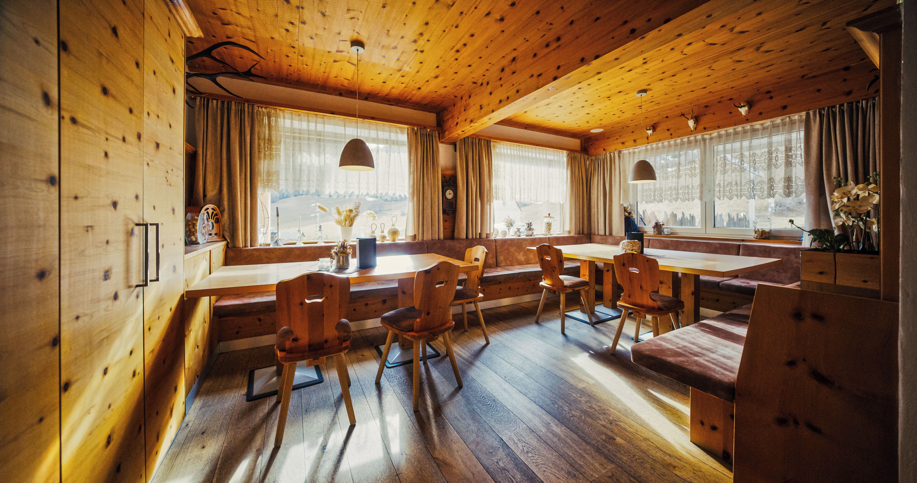 A wooden interior with a dining area, wooden chairs, a table, and a bench.