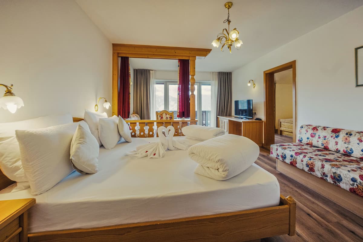 Une chambre d’hôtel avec un grand lit, un bureau avec une télévision, un canapé et un lustre.