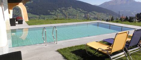 Piscina con vistas a las montañas, mobiliario exterior y una pérgola.