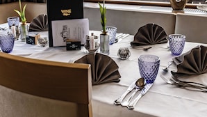 A dining table set with a menu, cutlery, and glassware, with a mountain view through a window. - Sporthotel Kalcherhof (Racines)