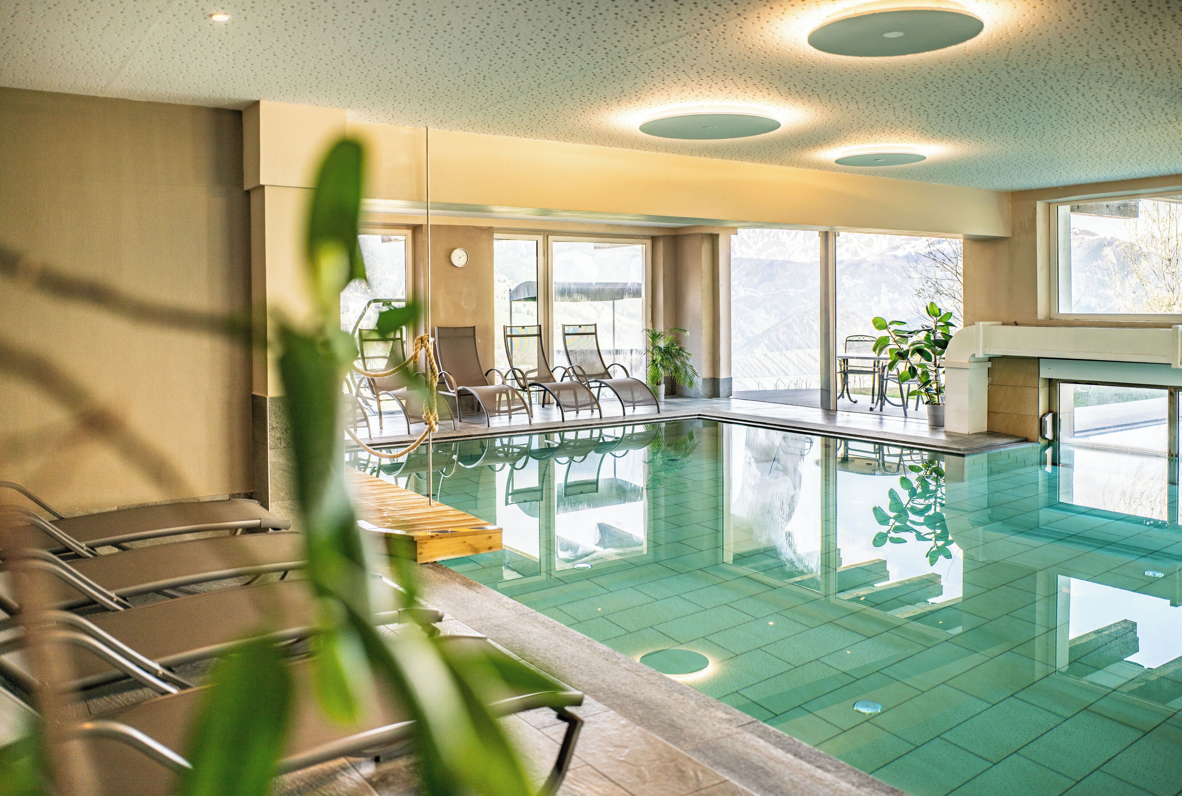 Una piscina interna con pareti in vetro trasparente, poltrone relax e piante in vaso.