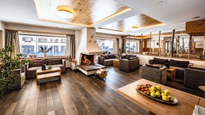 A modern living room with a fireplace, wooden flooring, and a large window. - Sporthotel Kalcherhof (Racines)