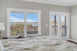 Un dormitorio con una cama grande, una ventana con persianas, una puerta con vistas y una lámpara en una mesita de noche.