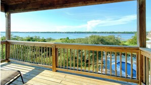 Eine Holzterrasse mit Geländer, die auf einen Swimmingpool und ein Gewässer mit Blick blickt.