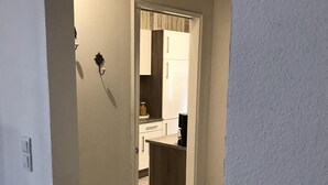 Un couloir mène à une cuisine dotée d’un plancher en bois et de meubles blancs.