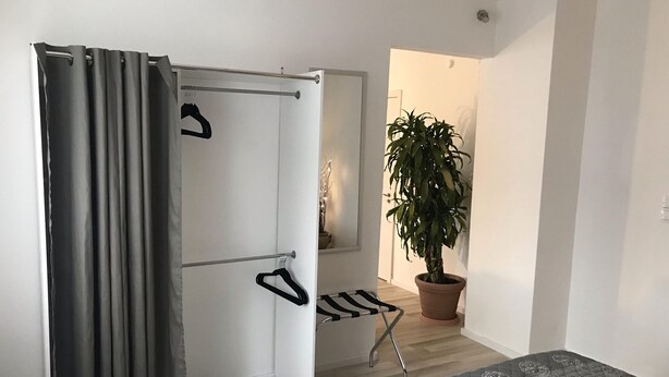 Une chambre à coucher de taille réduite, comprenant un lit, un fauteuil suspendu, une plante en pot et une porte coulissante.