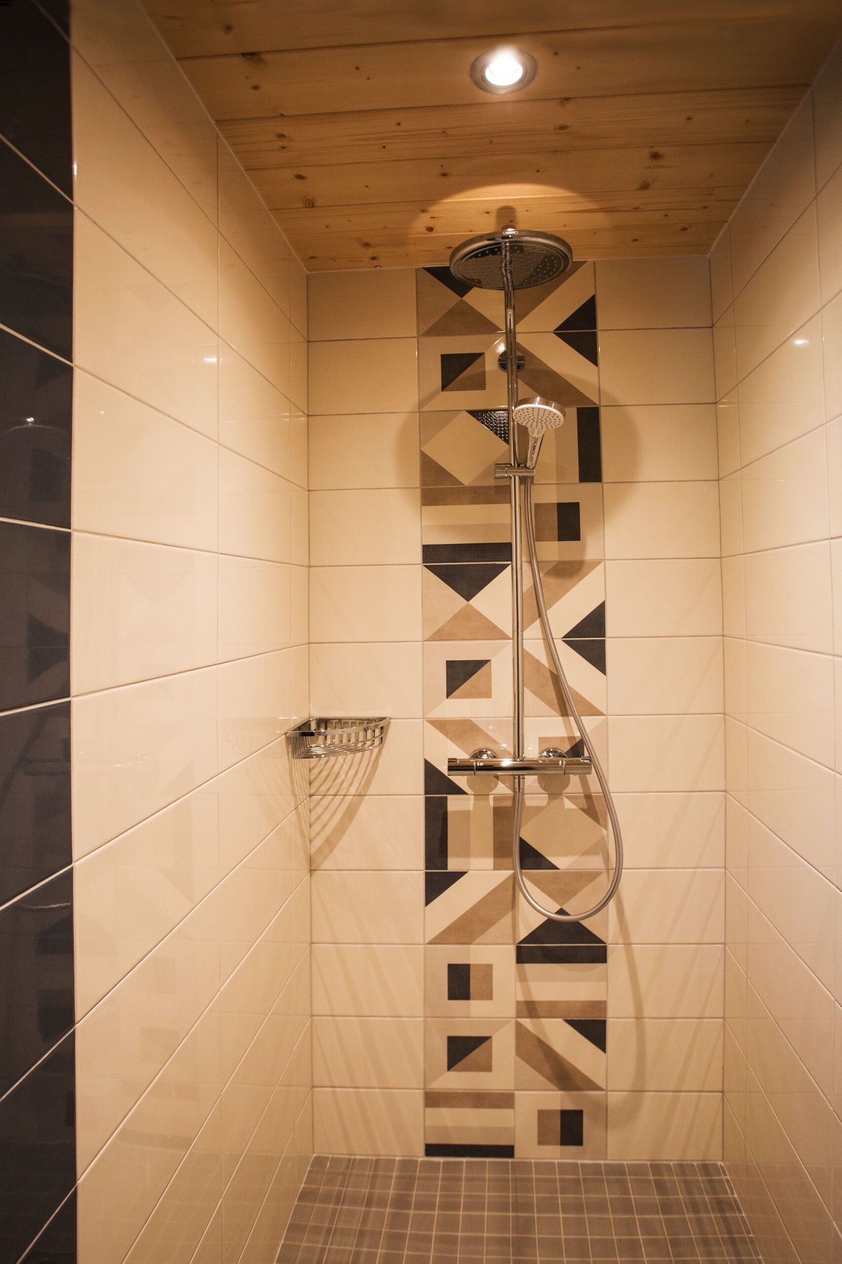 A shower with a geometric tile pattern on the walls and a wooden ceiling.