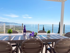 An outdoor dining area with a table and chairs, a potted plant, and a view of the sea and cityscape. - VillaTierra. Luxury villa. Best Views in Nerja (Nerja)