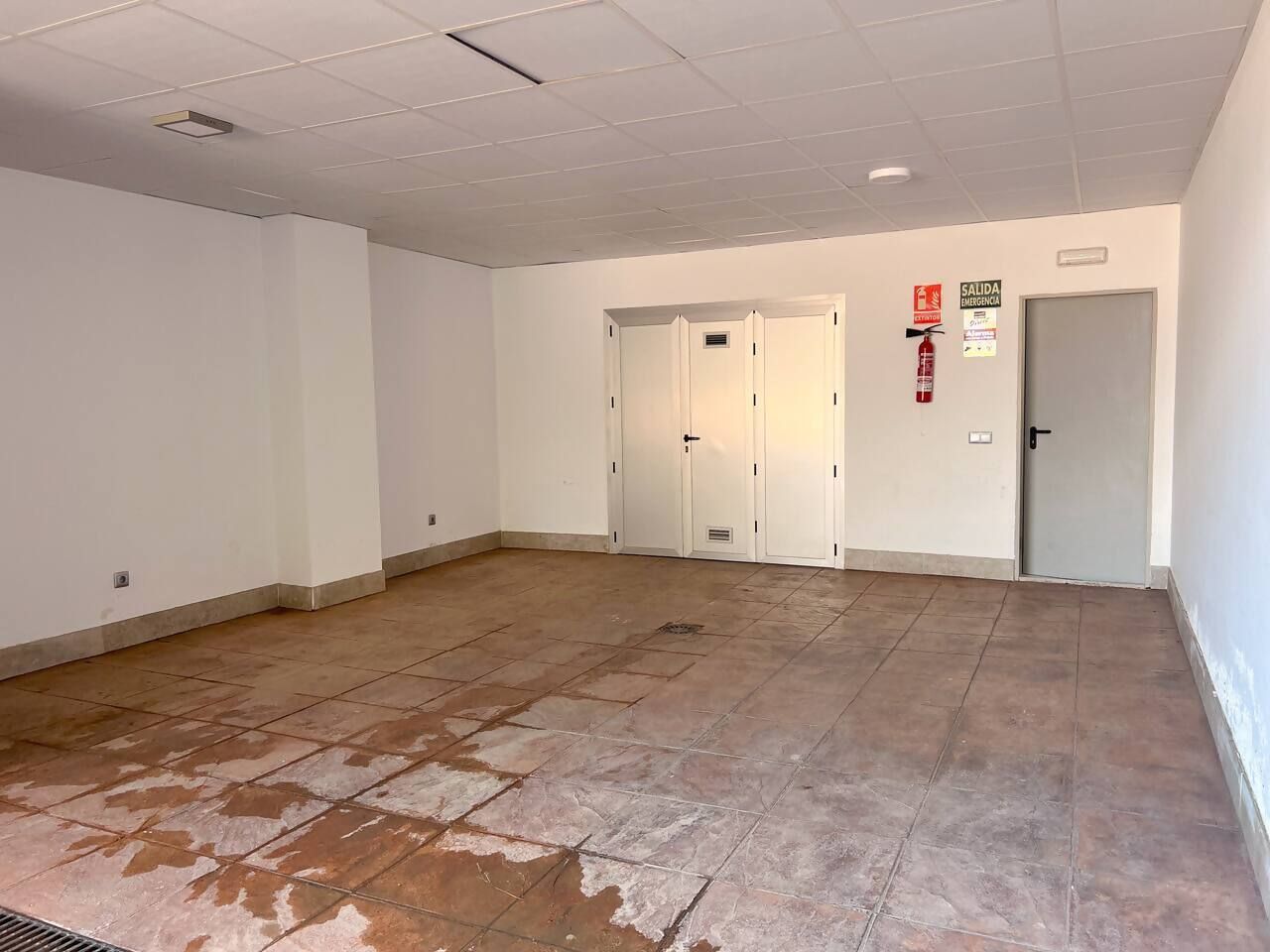A spacious room with a tiled floor, white walls, and a door with a fire extinguisher sign.