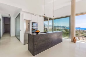 A modern kitchen with a central island, a built-in oven, and a large window offering a city view. - VillaTierra. Luxury villa. Best Views in Nerja (Nerja)