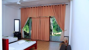 Un dormitorio con cama, espejo, una mesita de noche con un florero, y vista a un jardín a través de una puerta corredera.