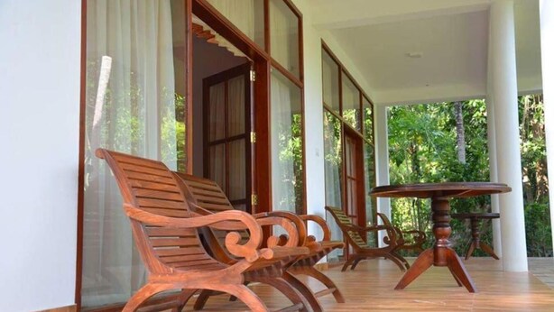 Un área de estar techada al aire libre con bancos de madera y una mesa redonda, rodeada de amplias ventanas.