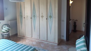 Une chambre à coucher avec une grande armoire, un lit recouvert d’une couvre-lit à rayures, une chaise et un luminaire suspendu.