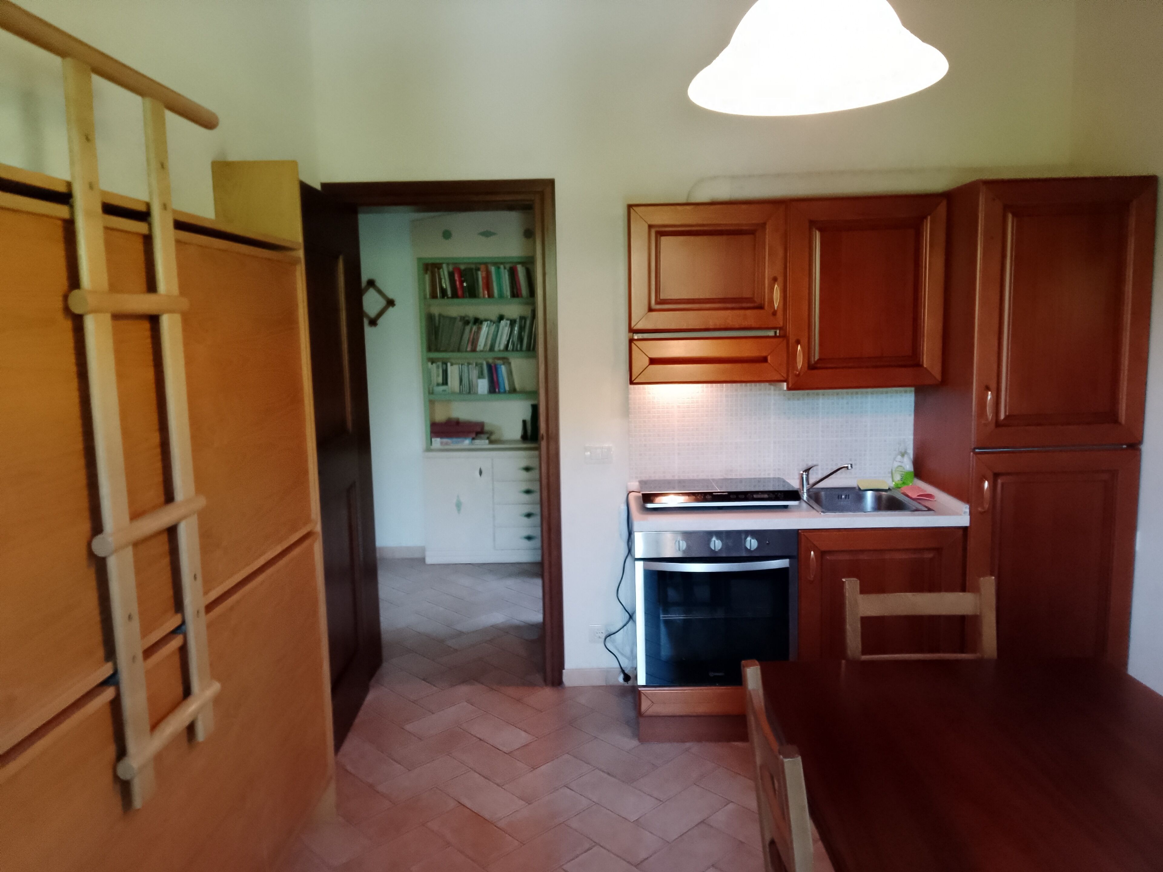 Una cucina con mobili in legno, un fornello e una libreria sullo sfondo.